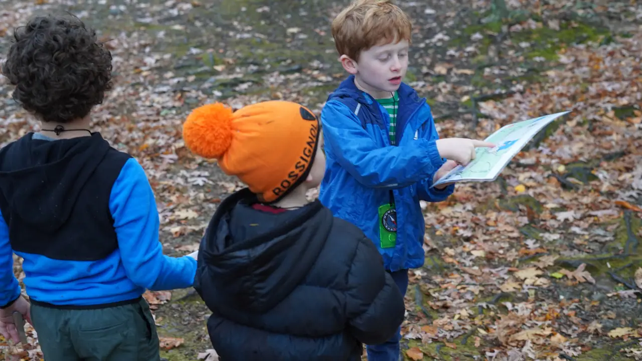 Three kids study a map together in the woods.